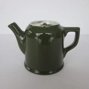 May include: A dark green ceramic teapot with a white lid and a handle. The teapot is glossy and has a rounded shape.