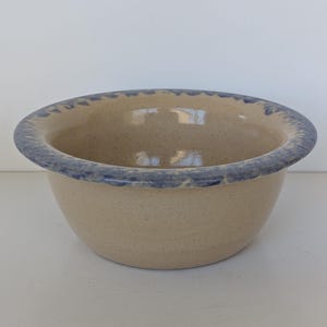 Może przedstawiać: Beżowa ceramiczna miska z niebieską obwódką. Misa ma nakrapianą fakturę i zaokrąglony kształt. Niebieska obwódka ma falisty wzór. Misa jest prawdopodobnie przeznaczona do serwowania lub mieszania.