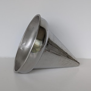 May include: A stainless steel conical sieve with a wide rim. The cone is perforated with small holes for straining liquids. The sieve is angled, highlighting its shape and construction, suitable for kitchen use.