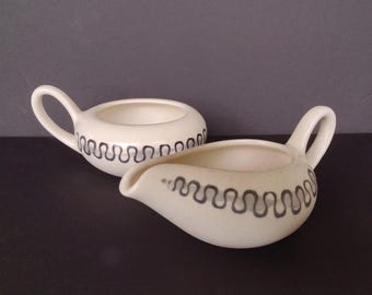 May include: A set of two white ceramic creamer and sugar bowls with a black wavy design around the rim.