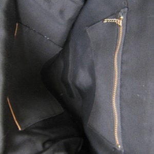 May include: The inside of a black tote bag with a zippered pocket. The pocket has a gold zipper pull.