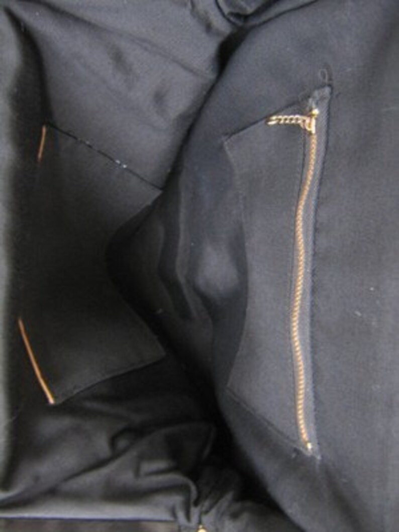 May include: The inside of a black tote bag with a zippered pocket. The pocket has a gold zipper pull.