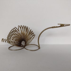 Peut inclure: Une bobine de ressort en métal doré avec un clip à l'extrémité. La bobine de ressort est en forme d'escargot et présente un design décoratif.