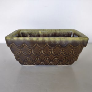 May include: A rectangular ceramic planter with a green and brown glaze. The planter has a scalloped design around the rim and a textured pattern on the sides.