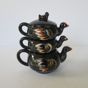 Może przedstawiać: Zestaw trzech czarnych ceramicznych czajniczków z ptasimi uchwytami i pokrywkami. Każdy czajniczek zdobi kolorowy wzór kwiatowy.