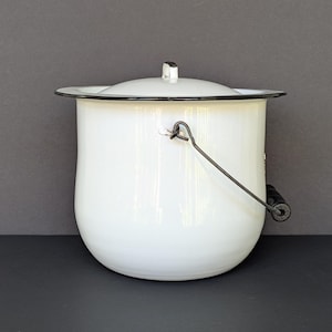 Può includere: Una pentola in smalto bianco con coperchio abbinato, caratterizzata da un bordo nero e un manico in metallo con impugnatura in legno nero. Il contenitore cilindrico presenta un bordo largo e piatto con una finitura liscia e lucida.