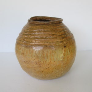 May include: A round, brown ceramic vase with a textured, rippled surface and a light yellow glaze. The vase has a wide opening at the top.