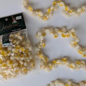 May include: A white and yellow garland, with a package of the same garland. The garland is made of small, round, white and yellow pieces. The package reads "Garland" and "9 feet (3 yds)".