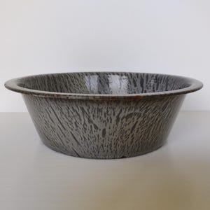 May include: A gray and white enamelware bowl with a speckled pattern. The bowl has a rounded shape with a slightly flared rim. The exterior has a mottled design, and the rim is a darker shade of gray.