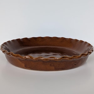 May include: A brown ceramic pie dish with a fluted edge. The dish is round and has a glossy finish. The pie plate is empty and ready for baking.