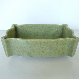 Puede incluir: Un macetero de cerámica verde con un acabado moteado. El macetero tiene una forma rectangular con bordes redondeados y un borde ligeramente elevado.