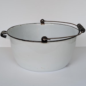 May include: A white enamelware pot with a black rim and handles. The pot has a metal handle that arches over the top, with black wooden grips. The pot is round and has two small side handles.
