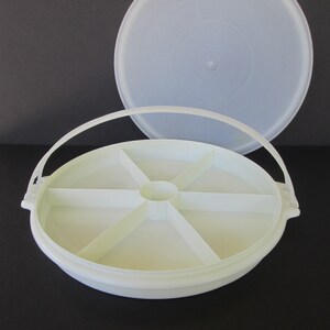 Op de afbeelding: Witte plastic serveerschaal met een deksel en een handvat. De schaal heeft zes vakken om snacks of hapjes in te bewaren.