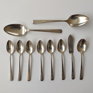 Può includere: Un set di dieci cucchiai d'argento, tra cui un coltello da burro e un cucchiaio da portata più grande. I cucchiai sono tutti lucidati e hanno un design classico.