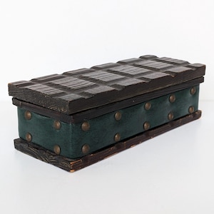 May include: A rectangular wooden box with a dark, textured lid and a green, studded fabric body. The box has a vintage aesthetic, with brass-colored studs and a dark brown wooden frame. The lid has a carved, grid-like pattern.