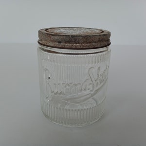Peut inclure: Un pot en verre transparent avec un motif côtelé et un couvercle en métal rouillé. Le pot est étiqueté "Sunsweet" en écriture cursive.