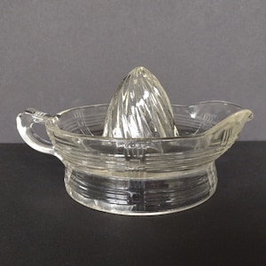 Op de afbeelding: Een heldere glazen citruspers met een geribbeld ontwerp. De pers heeft een handvat en een basis met een geribbeld patroon.