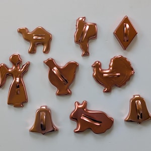 May include: A collection of copper-colored cookie cutters in various shapes, including a camel, angel, turkey, bell, and rabbit. These cutters are designed for creating festive treats.