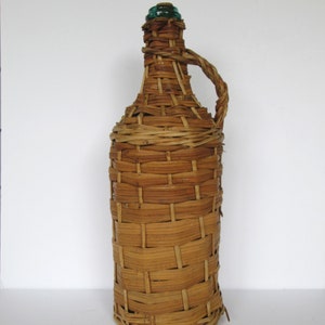 May include: A brown wicker-wrapped glass bottle with a green glass stopper. The bottle has a handle and is made of woven wicker.