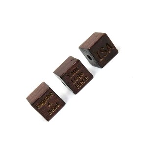 Puede incluir: Tres cuentas de madera en forma de cubo con diferentes grabados. La primera cuenta dice "Engrave A Bead", la segunda cuenta dice "Your Logo Here" y la tercera cuenta dice "ISA".