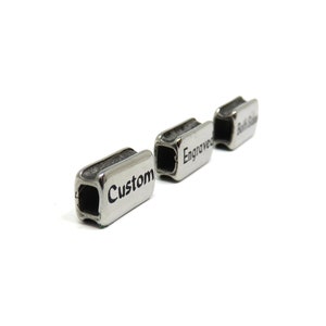 May include: Three silver metal rectangular beads with engraved text. The beads read "Custom", "Engraved", and "Soft Side".