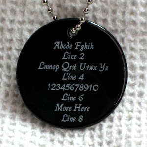 May include: A black round tag with a silver chain. The tag has white text that reads: Abcde Fghik Line 2 Lmnop Qrst Uvwx Yz Line 4 12345678910 Line 6 More Here Line 8