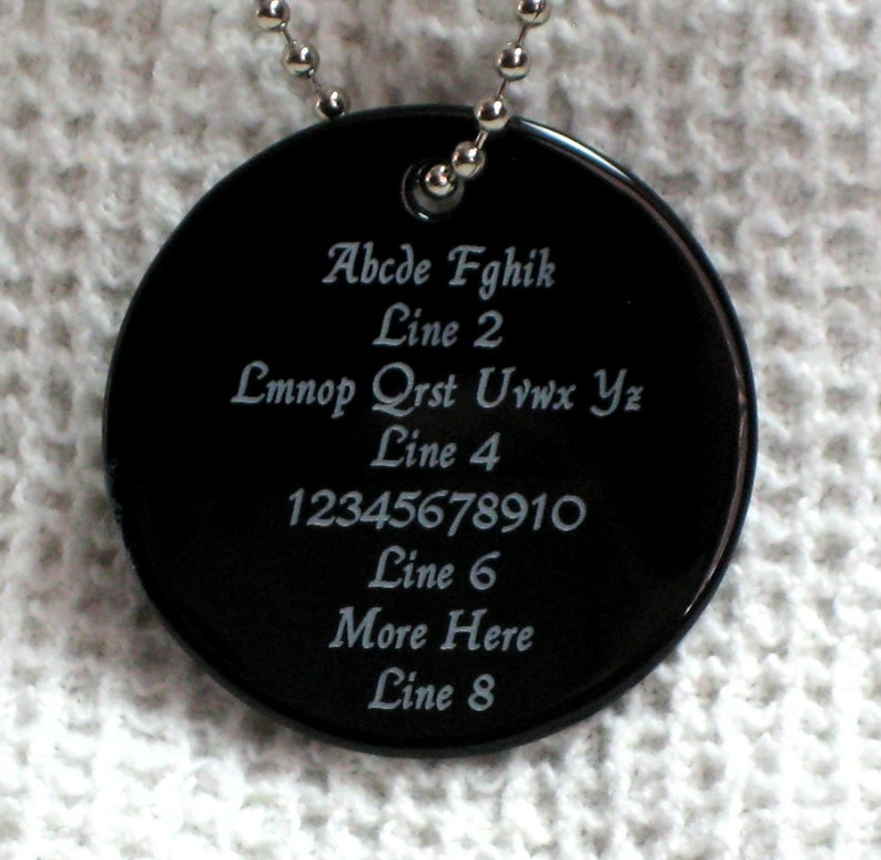 May include: A black round tag with a silver chain. The tag has white text that reads: Abcde Fghik Line 2 Lmnop Qrst Uvwx Yz Line 4 12345678910 Line 6 More Here Line 8
