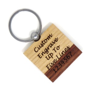 May include: A wooden keychain with a light brown top and a dark brown bottom. The top is engraved with the text "Custom Engrave Up To Five Lines". The bottom is engraved with the number "1234567".
