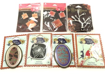 May include: Assortment of metal and plastic pendants on packaging cards. The pendants feature various designs, including an owl, a tree branch, and floral patterns. The cards are pink and white with the words "Bella Artiste" and "Heart & Soul".