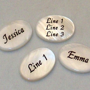 May include: Four white oval-shaped stones with black engraved text. The stones read "Jessica", "Line 1", "Line 1 Line 2 Line 3", and "Emma".