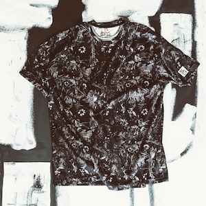 May include: Black t-shirt with a white floral pattern. The shirt has short sleeves and a crew neck. A small logo is visible on the sleeve. The fabric has a subtle sheen. The shirt is laid flat on a black and white surface.