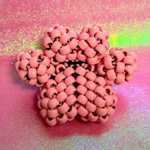 May include: A pink paw-shaped beaded keychain made of small, round beads. The beads are connected by a black string.