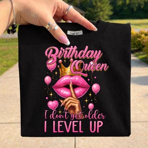 May include: Black t-shirt with a pink graphic that says "Birthday Queen" with a gold crown, pink lips, balloons, and the text "I don't get older I LEVEL UP".