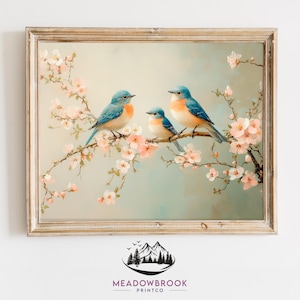Puede incluir: Una impresión enmarcada que presenta tres pájaros azules posados en una rama floreciente con flores rosas. Los pájaros tienen plumas azules y pechos naranjas. La impresión tiene un fondo azul claro y beige y un marco dorado. El logotipo de Meadowbrook Printco está en la parte inferior.