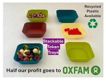 May include: Five square plastic trays in different colors, including green, blue, yellow, red, and brown. The trays are stacked on top of each other. The text "Stackable Token Trays" is written in purple on a white background. The text "Recycled Plastic Available" is written in black on a white background. The text "Half our profit goes to OXFAM" is written in black on a white background. The text "OXFAM" is written in black on a white background with a green recycling symbol next to it.