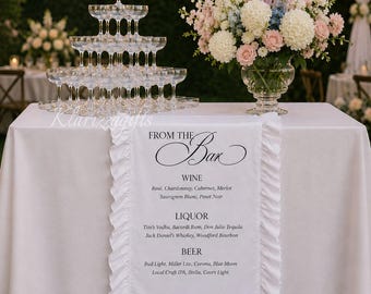 May include: A wedding reception bar setup with a white tablecloth, a champagne glass tower, and a floral arrangement. A white runner with the text "FROM THE Bar" lists wine, liquor, and beer options.