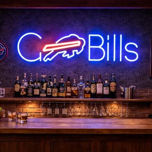 Puede incluir: Un bar en casa con un letrero de neón "Go Bills", una camiseta enmarcada y una colección de botellas de licor. El bar cuenta con una encimera de madera, taburetes de cuero y un pequeño refrigerador. También se ve un casco de fútbol americano y un cuenco de limas.