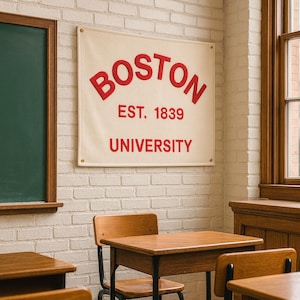 Puede incluir: Una pancarta color crema con la palabra "BOSTON" en rojo, arqueada en la parte superior, y "EST. 1839" y "UNIVERSITY" debajo. La pancarta está colgada en una pared de ladrillos blancos en un aula.