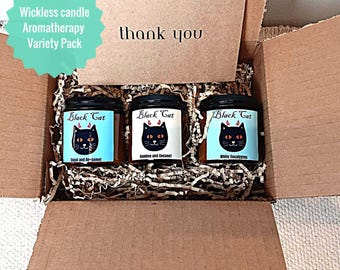 May include: An open cardboard box containing three wickless aromatherapy candles in glass jars with black lids. Each jar has a label with a black cat graphic and the words "Black Cat". The box also contains a card that says "thank you".