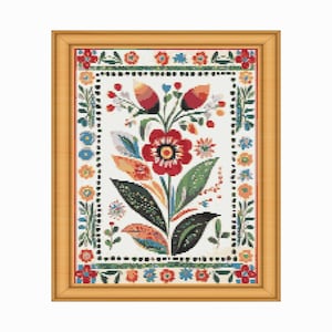 May include: A framed floral cross-stitch design. The artwork features a central red flower with a black center, surrounded by green leaves, and colorful accents. The border is adorned with small flowers in various colors, set against a white background.