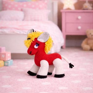 May include: A handmade red and white crochet horse toy with yellow mane and tail. The toy has black hooves and blue eyes. The horse is sitting on a pink polka dot rug in a child's bedroom.