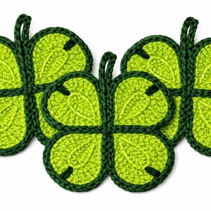 May include: A collection of five handmade, crocheted trivets in a four-leaf clover design. The trivets are a bright green color with a darker green border and stem, perfect for kitchen decor.