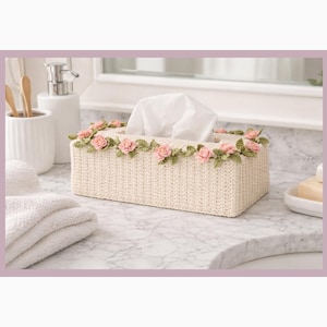 May include: A rectangular tissue box cover in a light beige woven pattern, adorned with pink and green floral embellishments. The box is filled with white tissues and sits on a marble countertop, suggesting a bathroom setting.