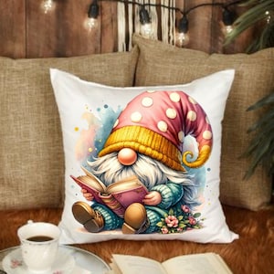 May include: White throw pillow with a watercolor-style illustration of a gnome wearing a pink and yellow hat reading a book. The gnome is sitting on a bed of flowers.