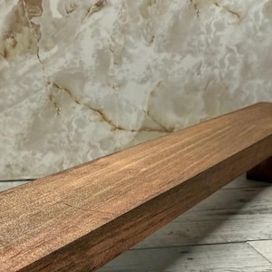 K&ouml;nnte beinhalten: Ein rechteckiges Holzregal mit einer mittelbraunen Beize und sichtbarer Holzmaserung. Das Regal hat gerade Kanten und eine glatte, flache Oberfl&auml;che und ist in einem Winkel dargestellt, der die Ober- und Vorderseite zeigt.