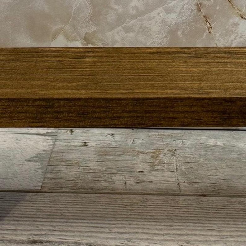K&ouml;nnte beinhalten: Ein rechteckiges Holzregal mit einer mittelbraunen Beize und sichtbarer horizontaler Holzmaserung. Das Regal hat eine glatte, flache Oberfl&auml;che und gerade Kanten, die die nat&uuml;rliche Textur und Farbe des Holzes deutlich zur Geltung bringen.