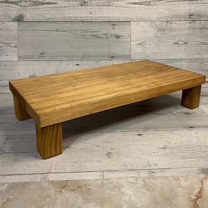 May include: A rectangular, wooden riser with a warm, honey-toned finish. The riser is supported by four sturdy, square legs, creating a stable platform. The wood grain is visible, adding to the natural aesthetic. This decorative piece is ideal for displaying items.