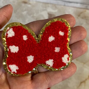 May include: Red and white polka dot bow with a gold glitter trim. The bow is made of a fuzzy fabric.