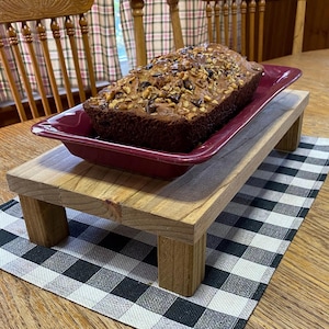 May include: A wooden serving stand with four legs, holding a red ceramic dish with a loaf of banana bread topped with walnuts and chocolate chips.