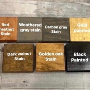 May include: Seven square wooden blocks arranged in two rows, each featuring a distinct finish and white text labels: Red chestnut Stain, Weathered gray stain, Carbon gray Stain, Gold painted, Dark walnut Stain, Golden oak Stain, and Black Painted.